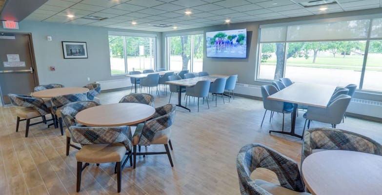 A spacious common area with tables and chairs and a large TV.