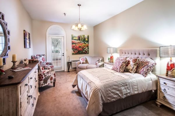 A well-furnished bedroom with a bed, chairs, and artwork.
