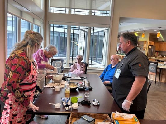 Residents and staff cooking together in a bright activity room