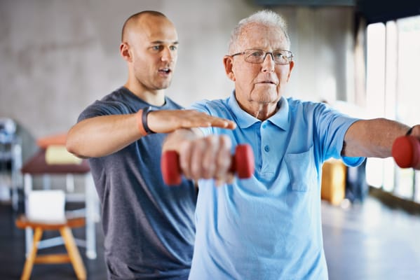 Resident exercising with a trainer using dumbbells