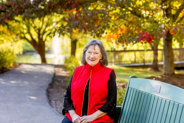 A smiling woman sitting on a bench in a colorful garden