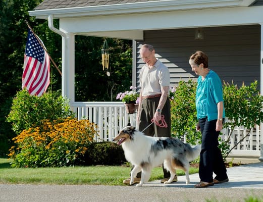 Couple walking a dog in front of a house