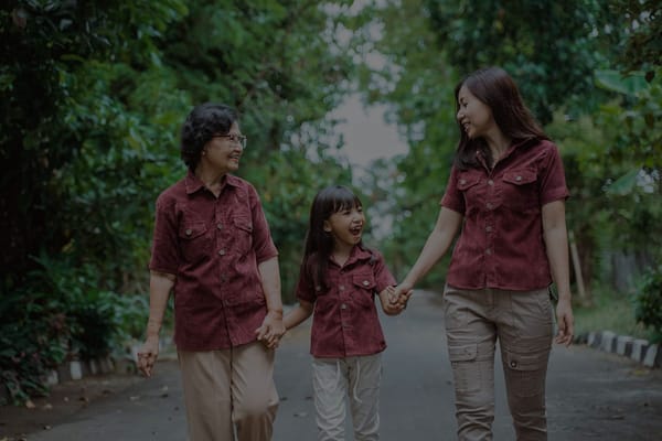 A woman and child walking with an elderly woman in a green outdoor area