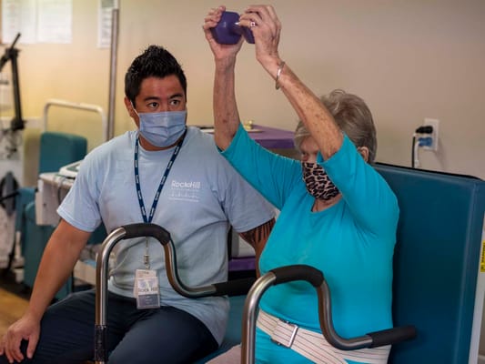 Staff assisting a resident with exercises in a therapy room