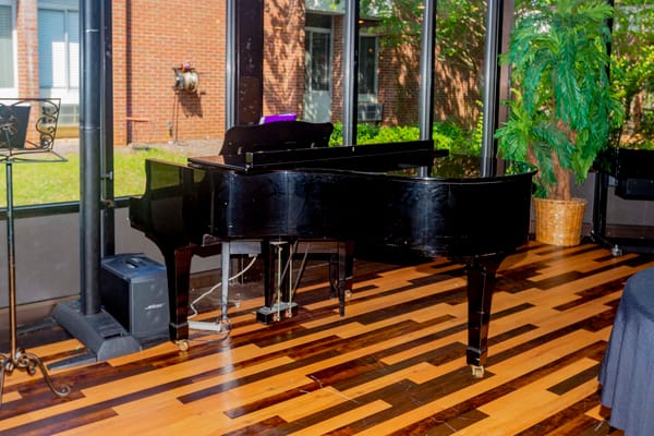A grand piano in a common area with large windows