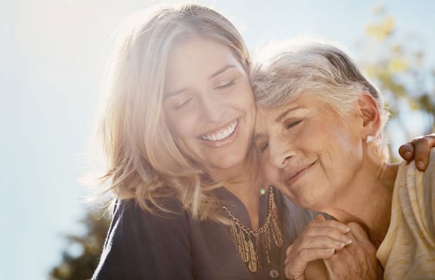 A caregiver happily embracing a senior resident outdoors