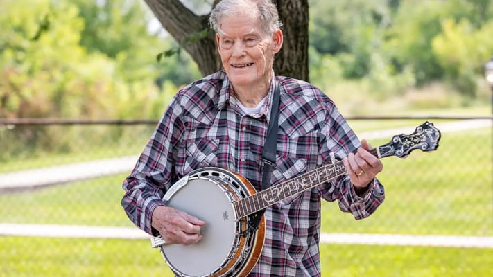 Elderly man playing a banjo outdoors