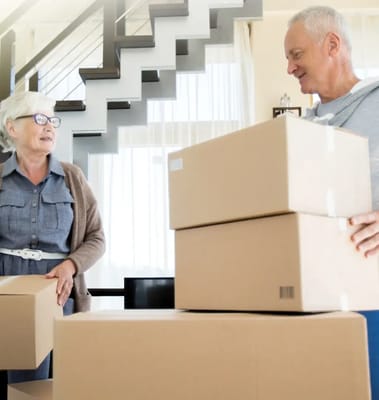 Two seniors interacting while handling moving boxes indoors