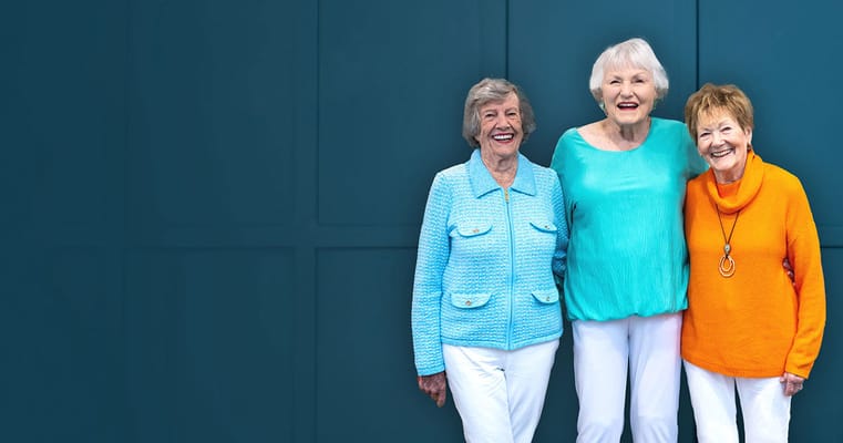 Three smiling women posing together in bright clothing