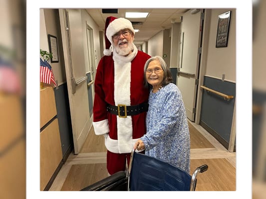 Resident smiling with Santa Claus in the hallway