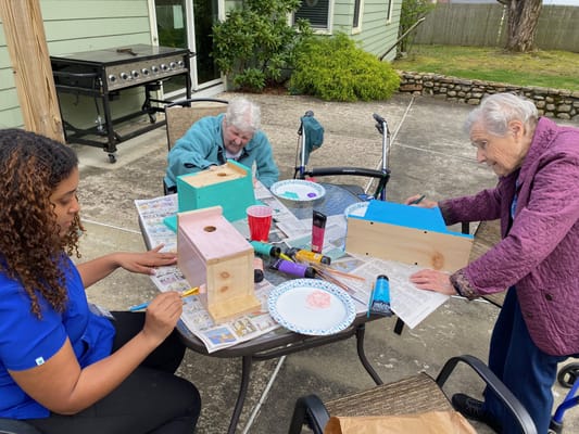 Residents and staff painting birdhouses outdoors
