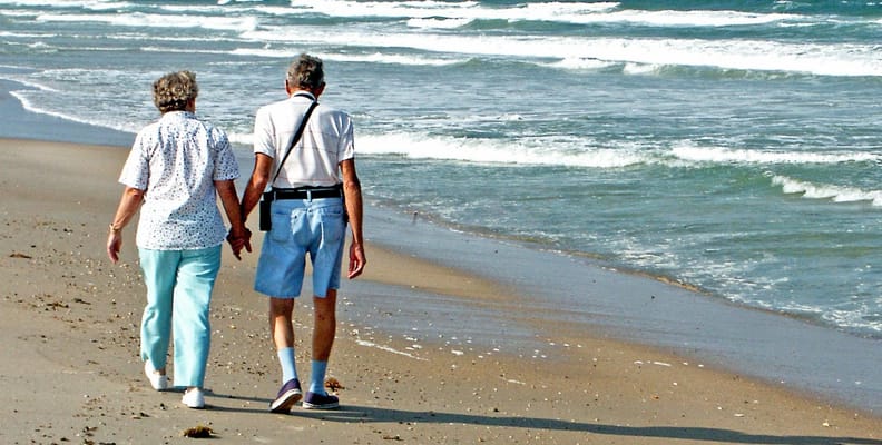 An elderly couple walking hand-in-hand along the beach