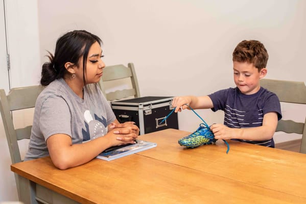 A caregiver and a child practicing tying shoes at a table