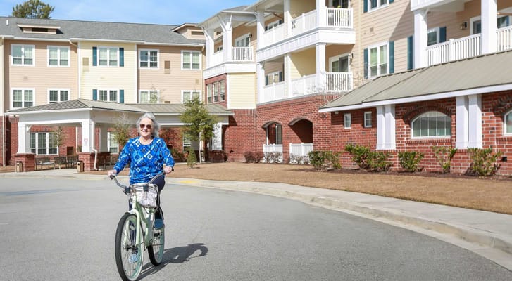 A smiling woman riding a bike outside the facility