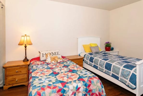 A cozy bedroom with two beds, a lamp, and a decorative quilt.