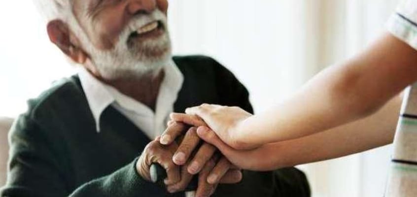 An elderly man smiling while holding hands with a younger person.