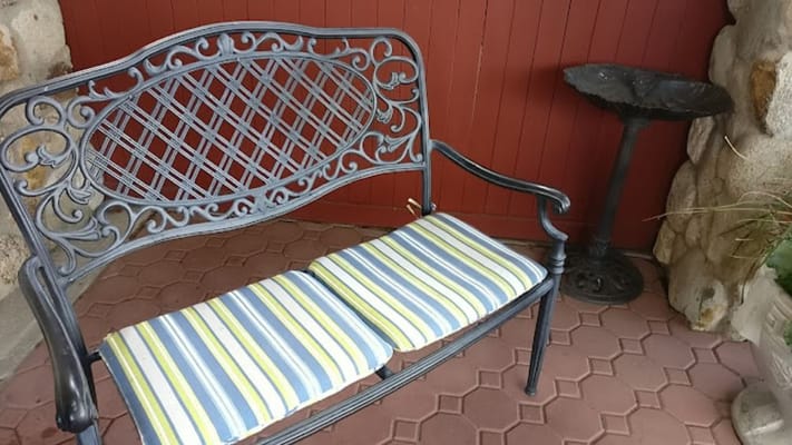 Vintage metal bench with striped cushions by a birdbath.