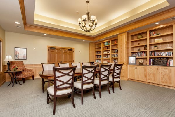 A dining room with a large table and wooden chairs, bookshelves in the background.