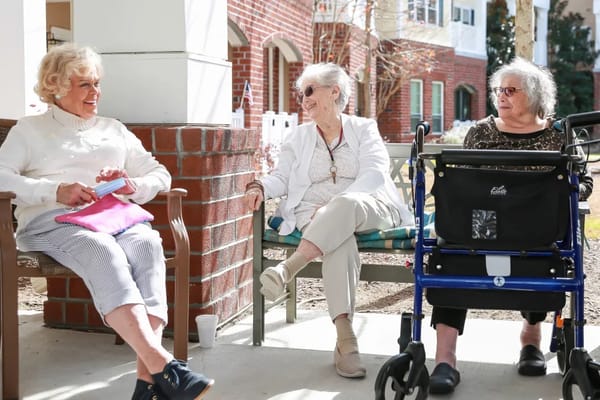 Three elderly women enjoying conversation outdoors in a sunny area