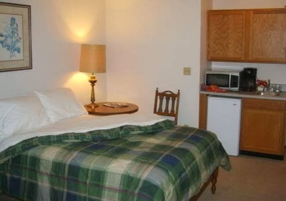 A cozy bedroom with a bed, a lamp, and a kitchenette.