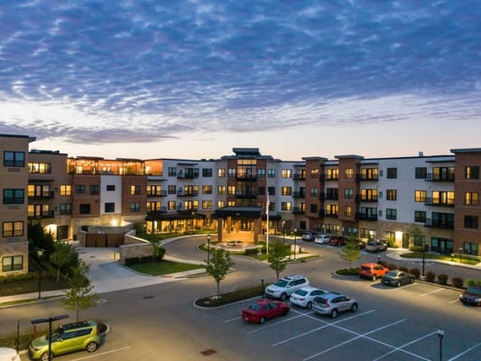 Aerial view of the exterior entrance and parking area of Rose Senior Living Carmel at dusk.