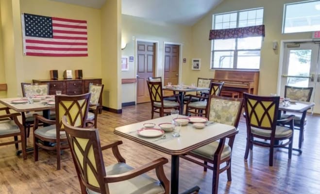 Bright dining room with tables set for meals and an American flag on the wall