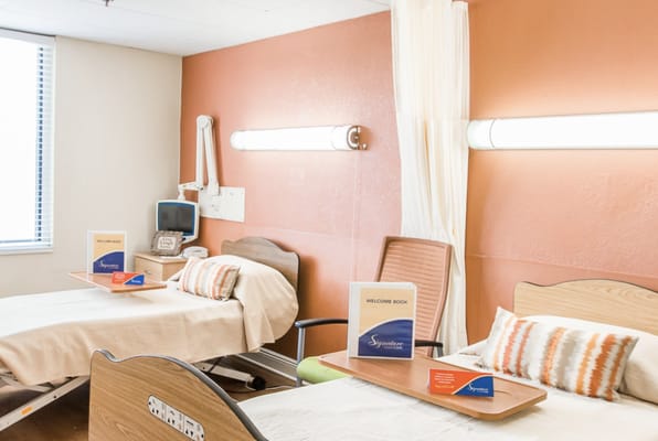 A bright patient room with two beds and welcome materials