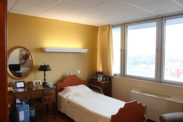A cozy bedroom with a single bed, desk, and large windows