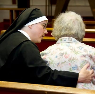 A nun comforting an elderly woman in a church setting