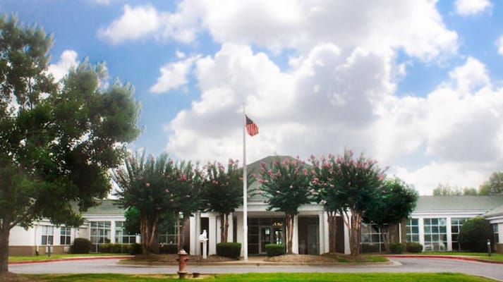 Exterior view of a senior living facility with trees and flag