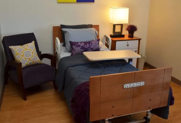 A well-furnished bedroom featuring a hospital bed, chair, and bedside table.