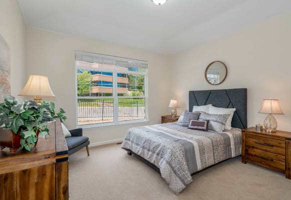 A bright and inviting bedroom with a bed, tables, and large windows.