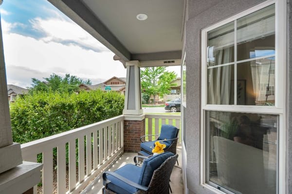 A view of the porch with two chairs and a landscaped front yard.