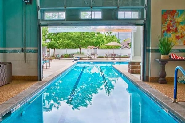 Indoor pool with open garage-style doors and outdoor seating area in view.