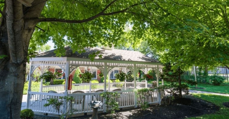 White gazebo surrounded by green trees and colorful flowers