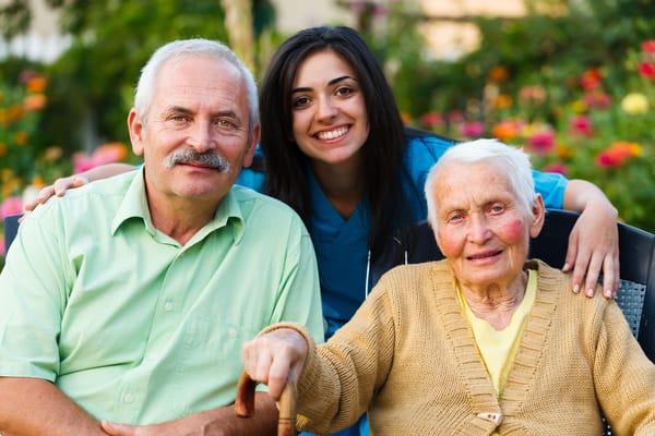 A smiling staff member with two senior residents outdoors