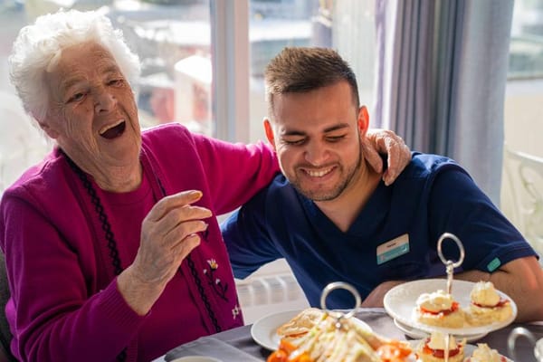 A resident and staff member share a joyful moment during tea.
