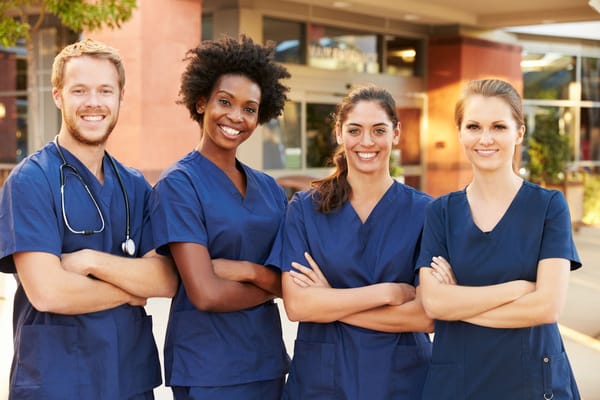 Four smiling healthcare staff in scrubs standing outdoors