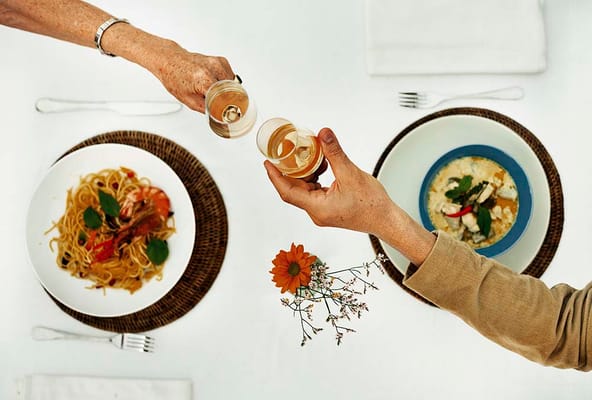 Two hands toasting over a meal at the dining table
