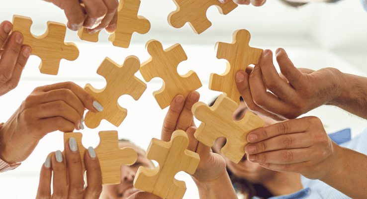 Group of hands assembling wooden puzzle pieces