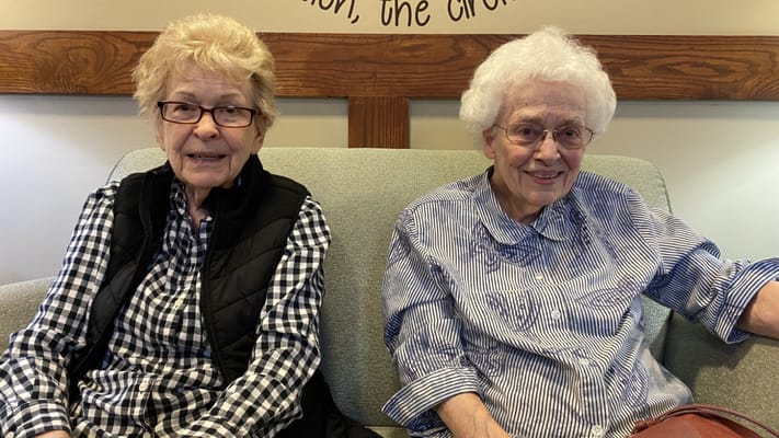 Two elderly women smiling on a couch in a common area