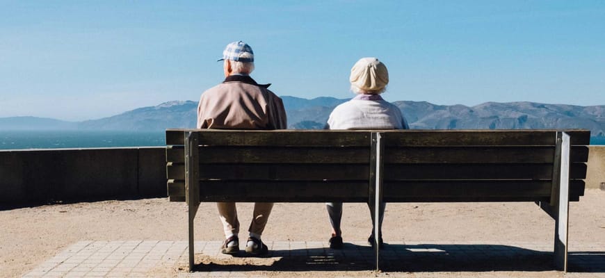 Two elderly individuals sitting on a bench outdoors