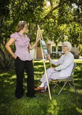 Care staff assisting a resident with painting outdoors
