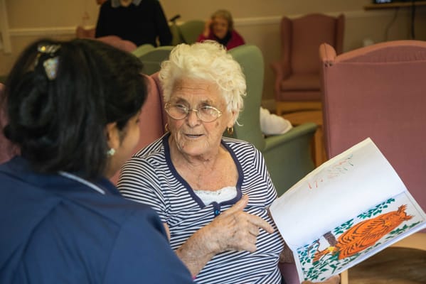 A resident engaged in conversation with a staff member while reading a book
