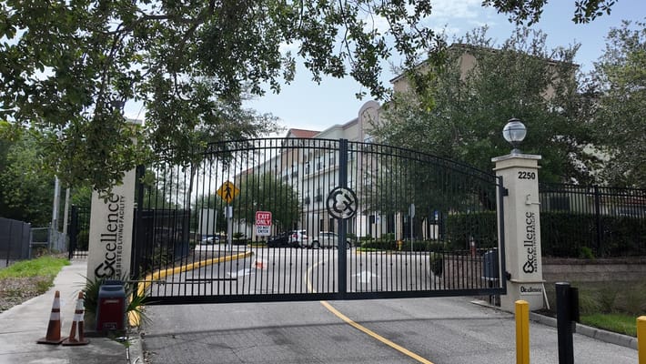 The gated entrance of Excellence Senior Living showing the facility name and roadway.