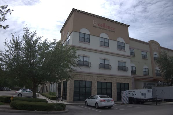 Front view of Excellence Senior Living facility with parking area.