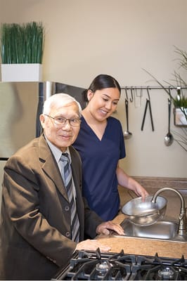 A caregiver assisting an elderly man in a kitchen