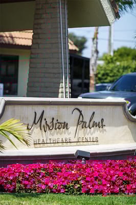 Sign of Mission Palms Healthcare Center with flowers