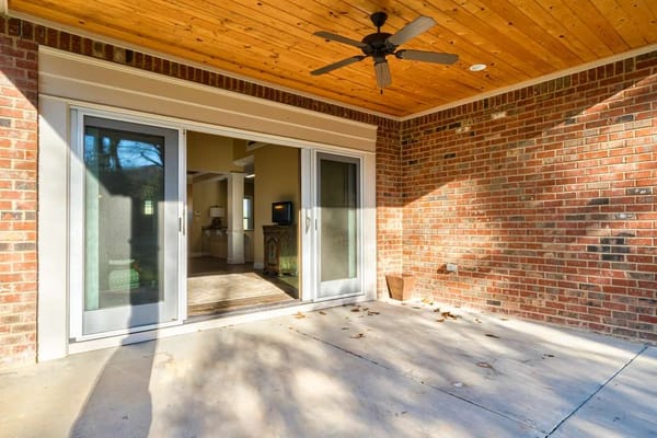 Covered outdoor patio area with brick wall and ceiling fan