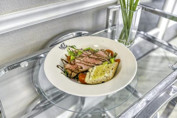 Plate with steak, salad, and bread on a glass table